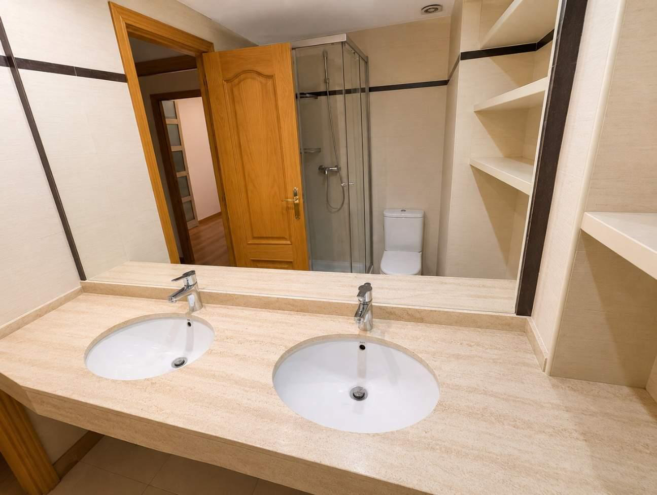 Baño con ducha de cristal y doble lavabo en mármol